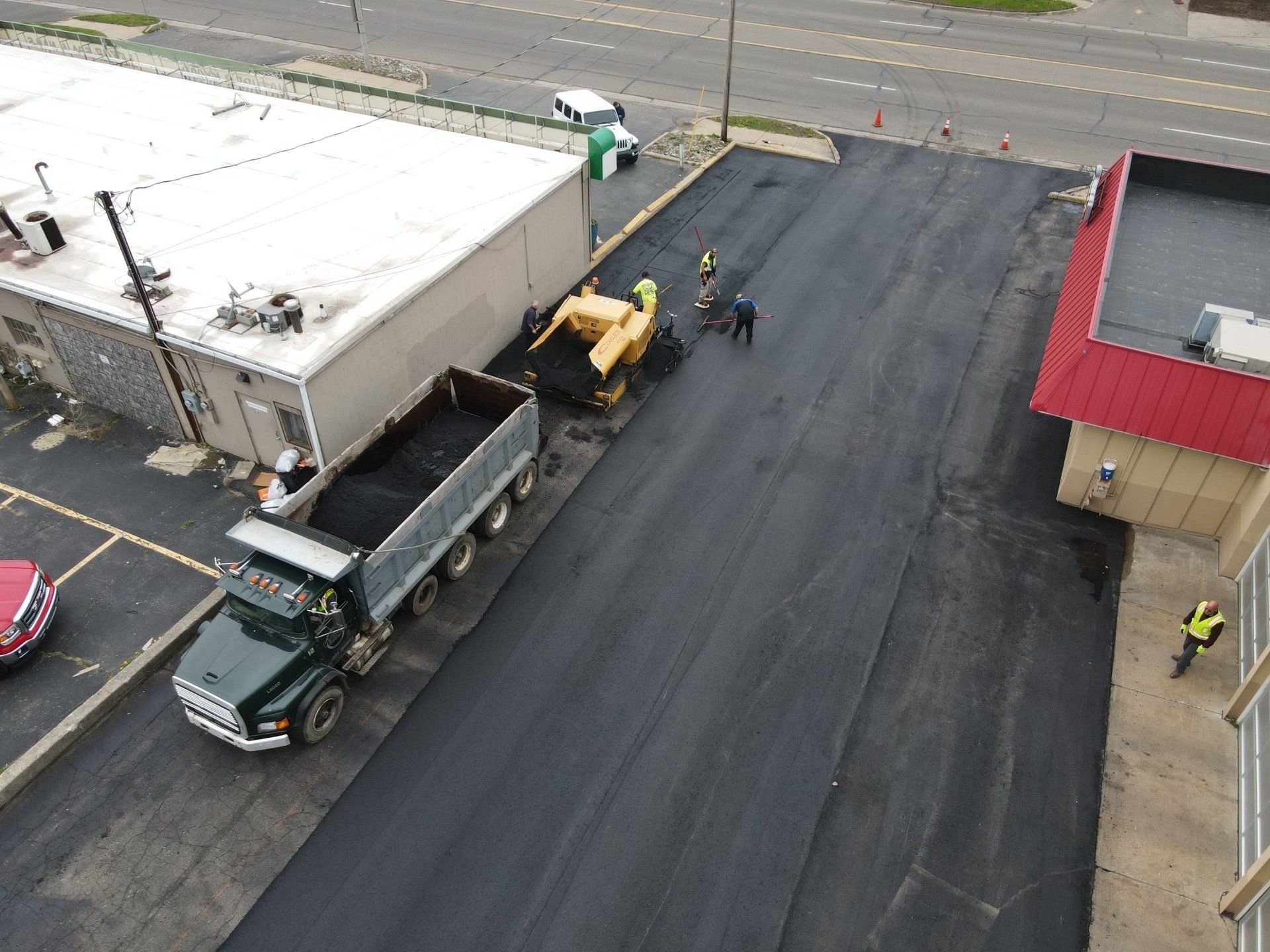 An aerial view of a dump truck being loaded with asphalt in a parking lot.