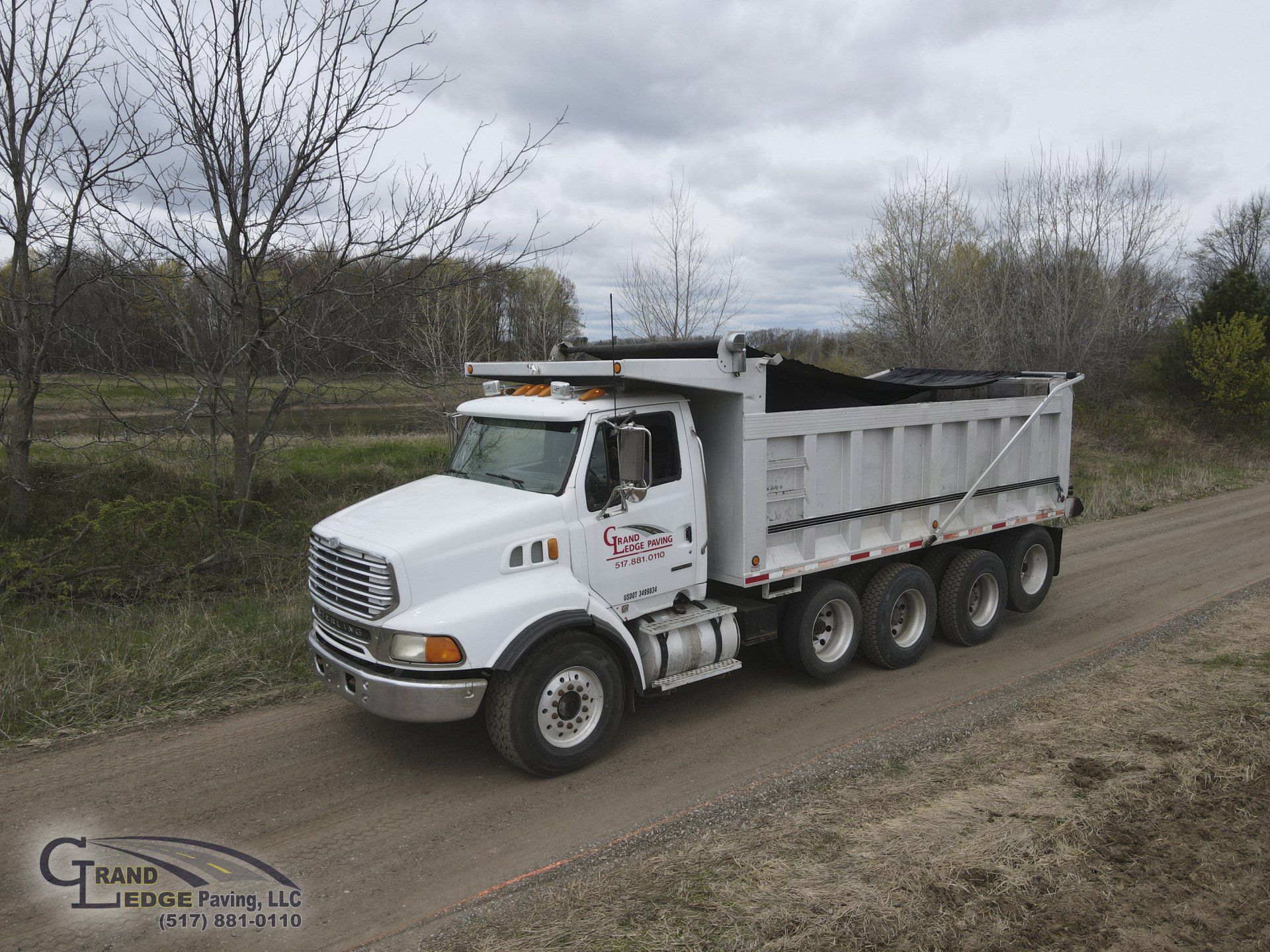 A white dump truck is driving down a dirt road
