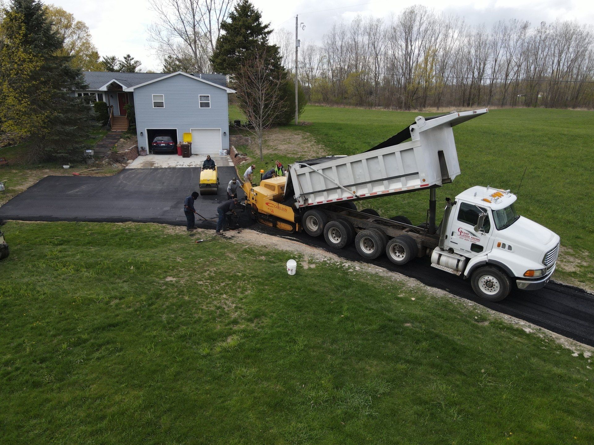 A dump truck is driving down a driveway next to a house.