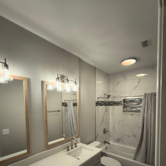 Bathroom with white marble tile shower, two mirrors, and vanity sink.