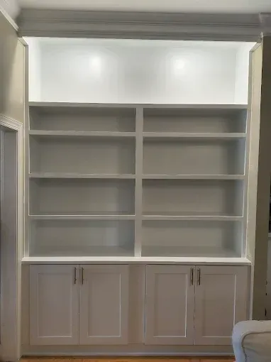 Built-in white bookshelf with shelves and cabinet doors, lit at top.