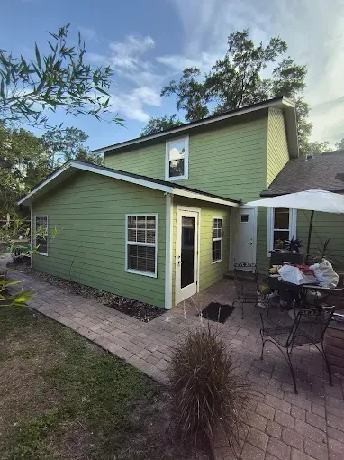Green two-story house with a brick patio, white door and windows, and a white umbrella.