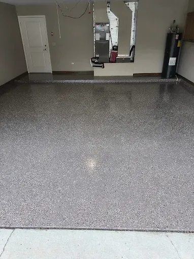 Garage with gray speckled epoxy floor and gray walls. Door on the left.