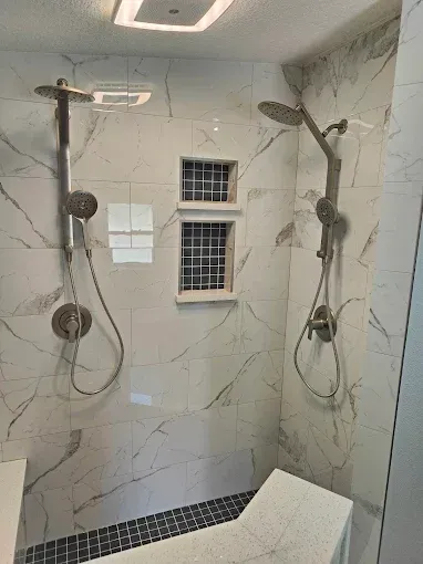 Two shower heads on marble-tiled wall, with built-in niches, and bench with dark tile floor.