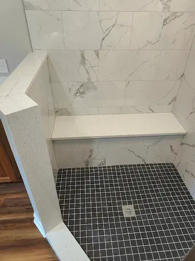 Tiled shower with black mosaic floor, white bench, and marble-look wall tiles.