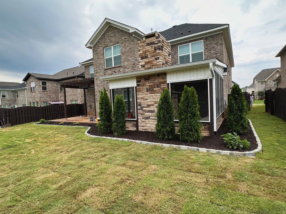 A large brick house with a screened in porch and a large lawn in front of it.