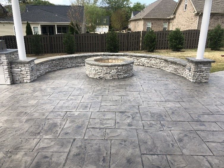 Decorative concrete patio with custom stone fire pit and seating wall in a Madison, AL backyard, showcasing premium outdoor living design.