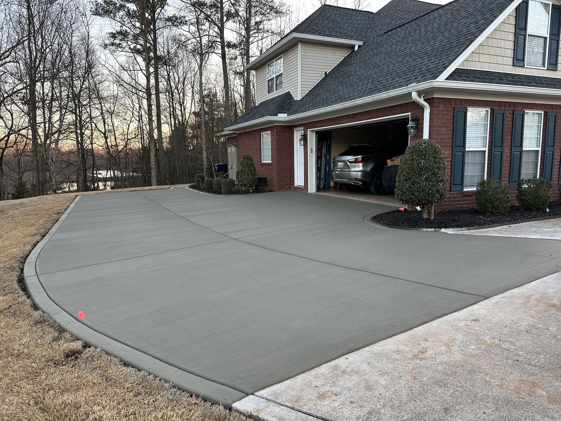 Newly poured concrete driveway next to a two-story brick house with a garage.