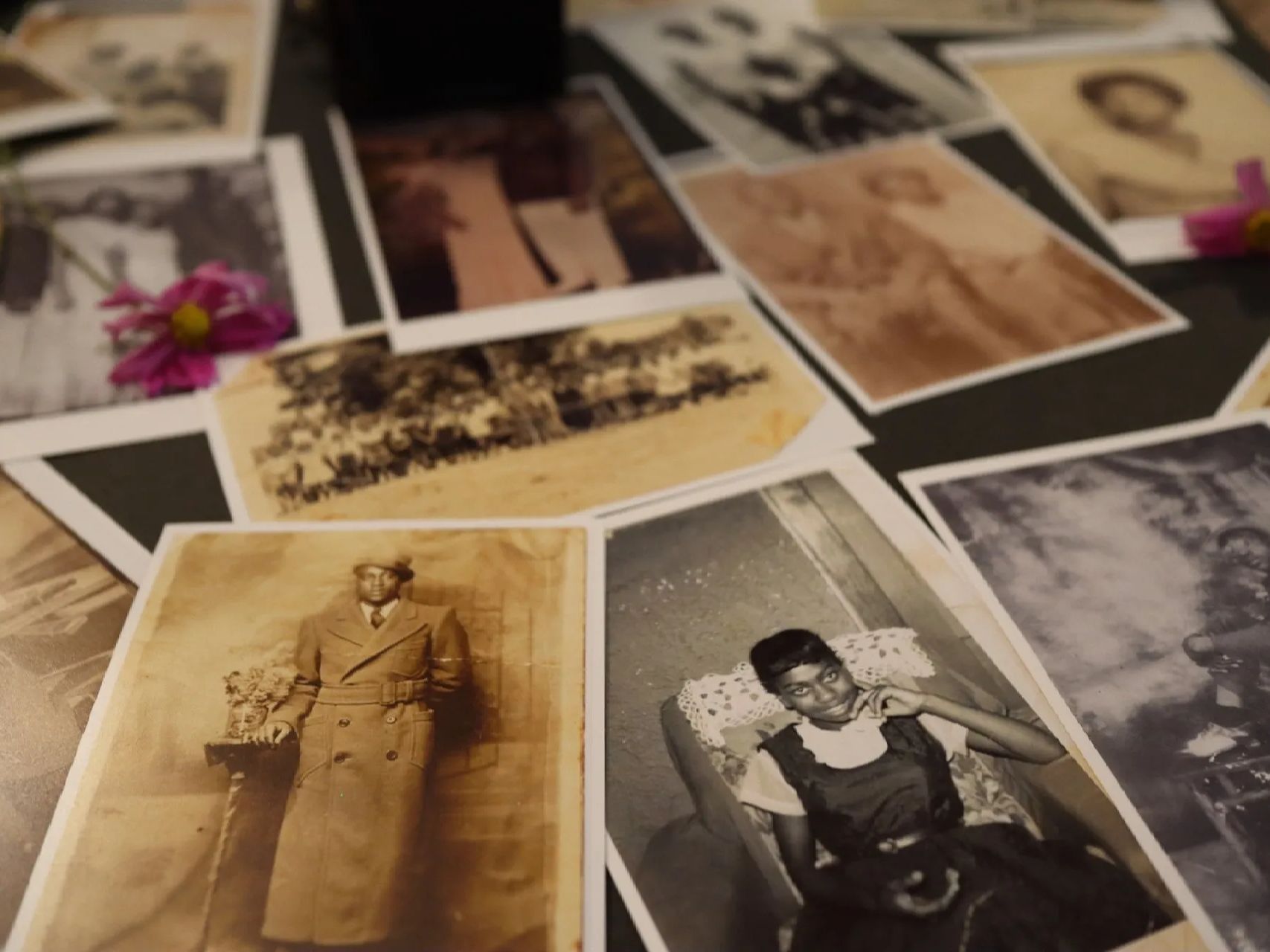 A man in a trench coat and a woman sitting in a chair are among many old photographs on a table