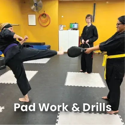 Person kicking a pad held by another during martial arts training in a dojo.