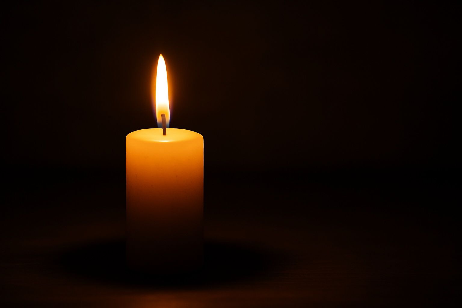 A single candle is lit in the dark.