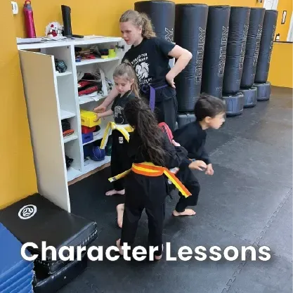 Martial arts class: Instructor guides students near storage. Black mats, bags, and yellow wall. 