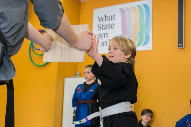 A young boy in a black karate uniform is being taught by a man.