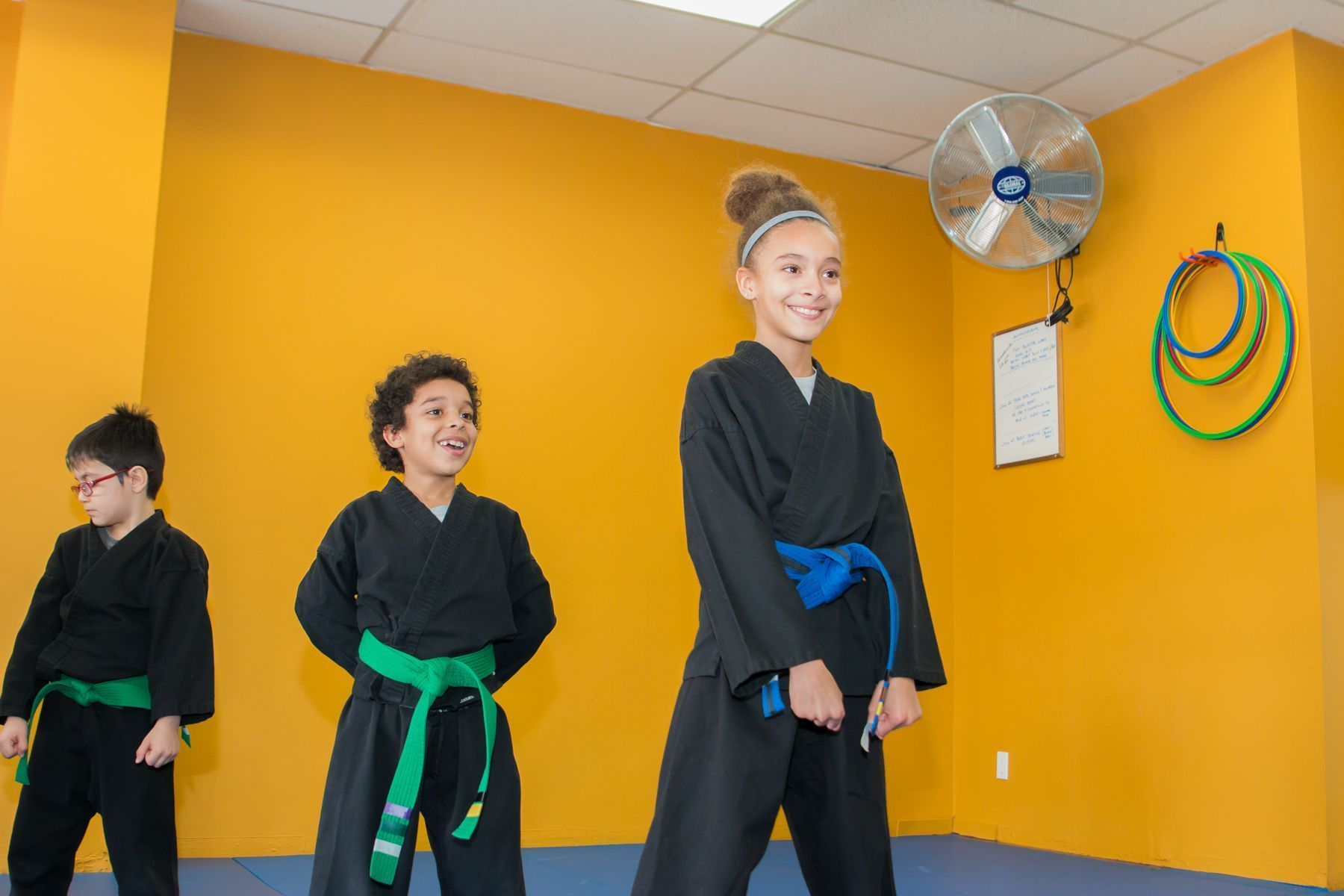 Three children in karate uniforms are standing in a room.