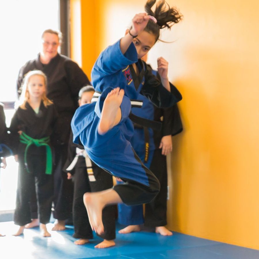 A woman in a blue karate uniform is jumping in the air
