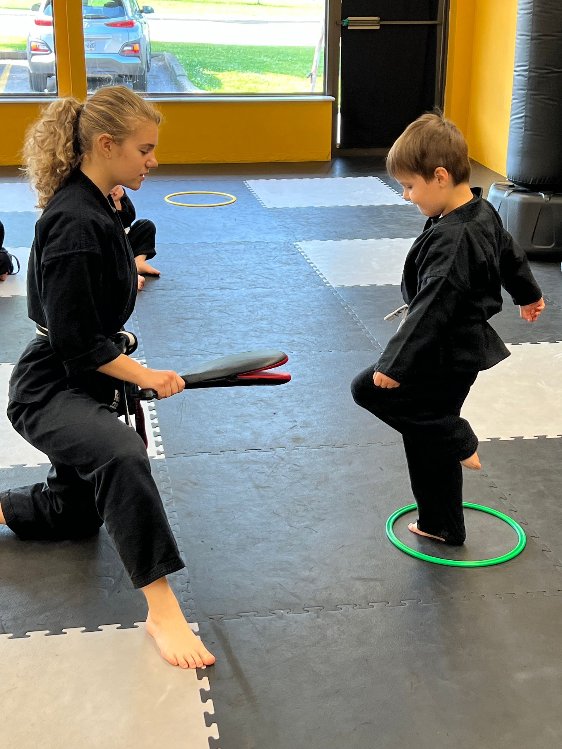 A young boy kicking a pad being held by a female karate instructor