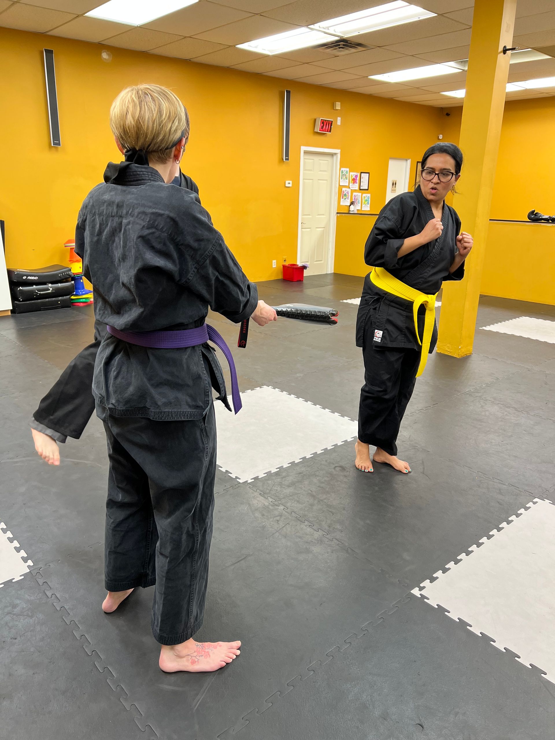 Two people in martial arts uniforms practice with a weapon in a dojo.