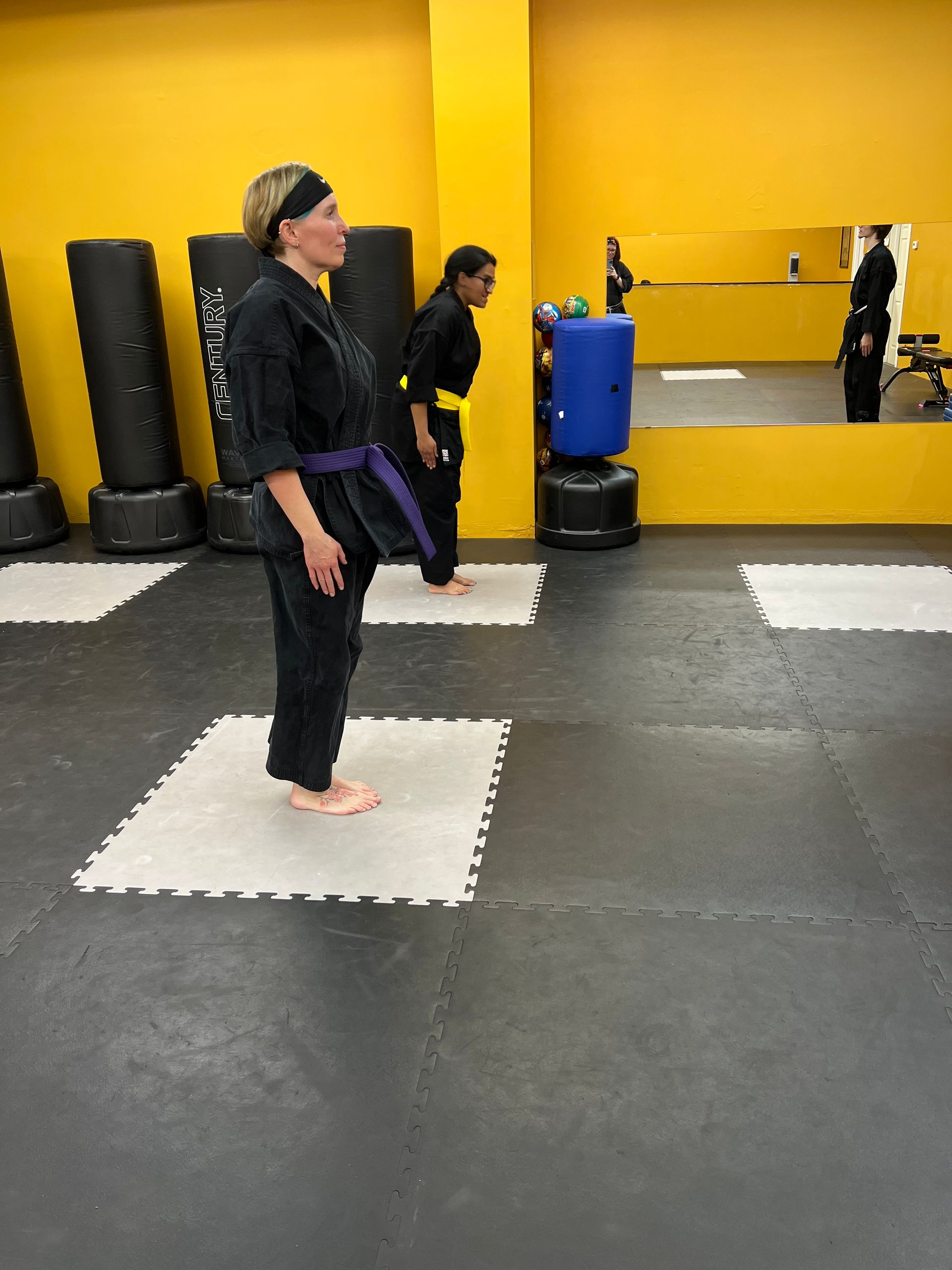 Two people in martial arts uniforms practice on mats in a dojo.