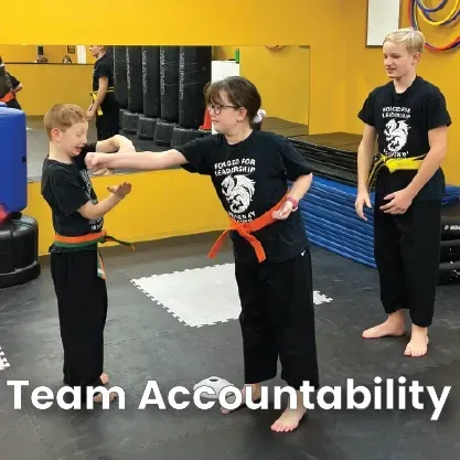 Karate students in black uniforms practice in a dojo, one giving high fives.