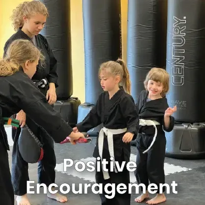 Karate students in black uniforms practice in a dojo, one giving high fives. 