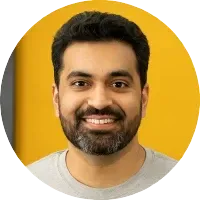 A man with a beard is smiling in front of a yellow wall.