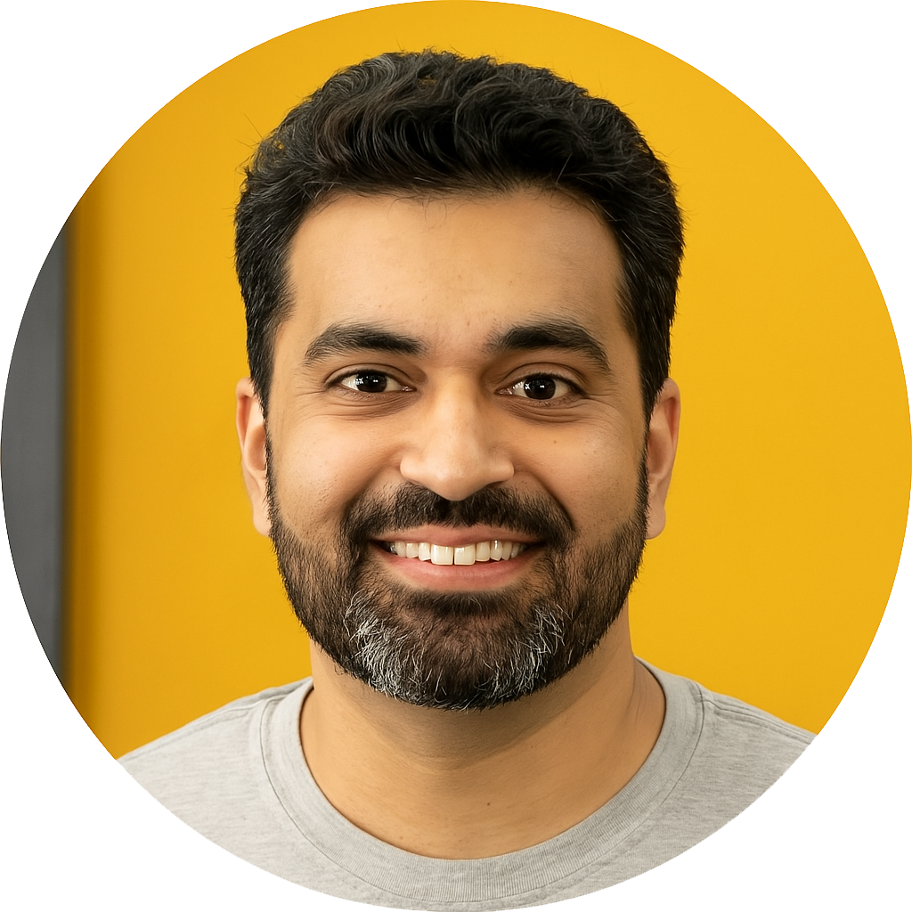 A man with a beard is smiling in front of a yellow wall.