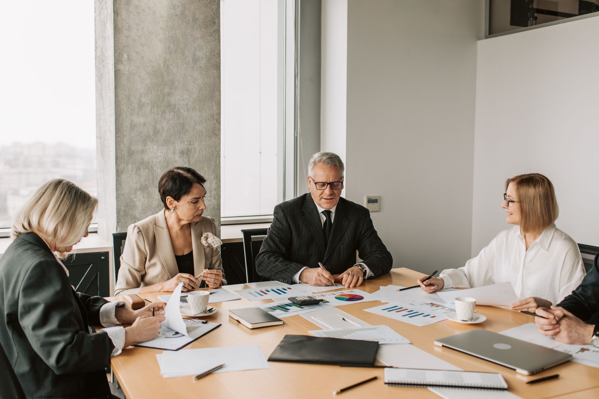 Business meeting with five people around a conference table reviewing documents and discussing plans