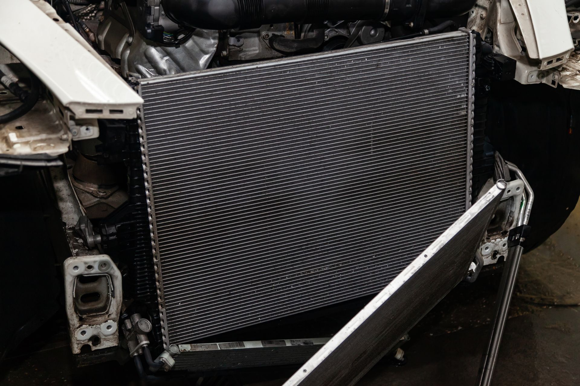 The front of a car with its bumper removed, exposing the radiator and air conditioning condenser in a workshop.