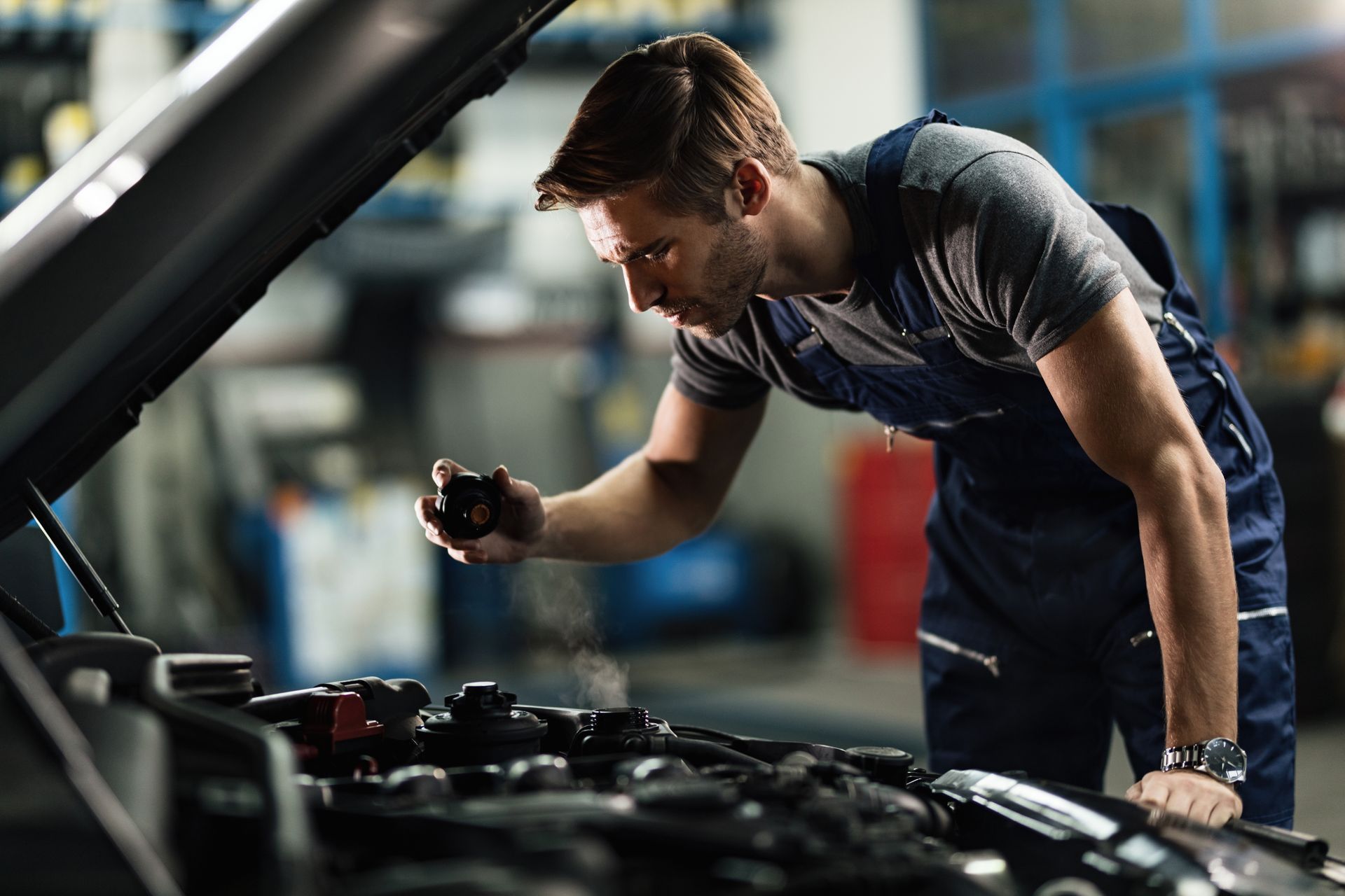 Mechanic spraying engine components under a car hood in a garage.
