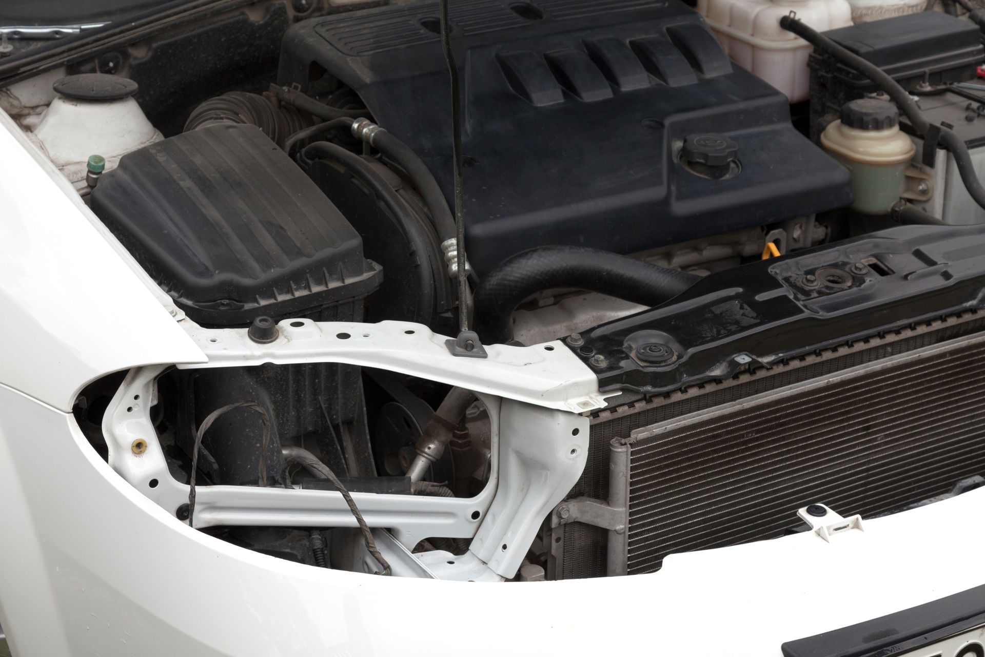 Car engine bay with headlight assembly removed. Black components, white body.
