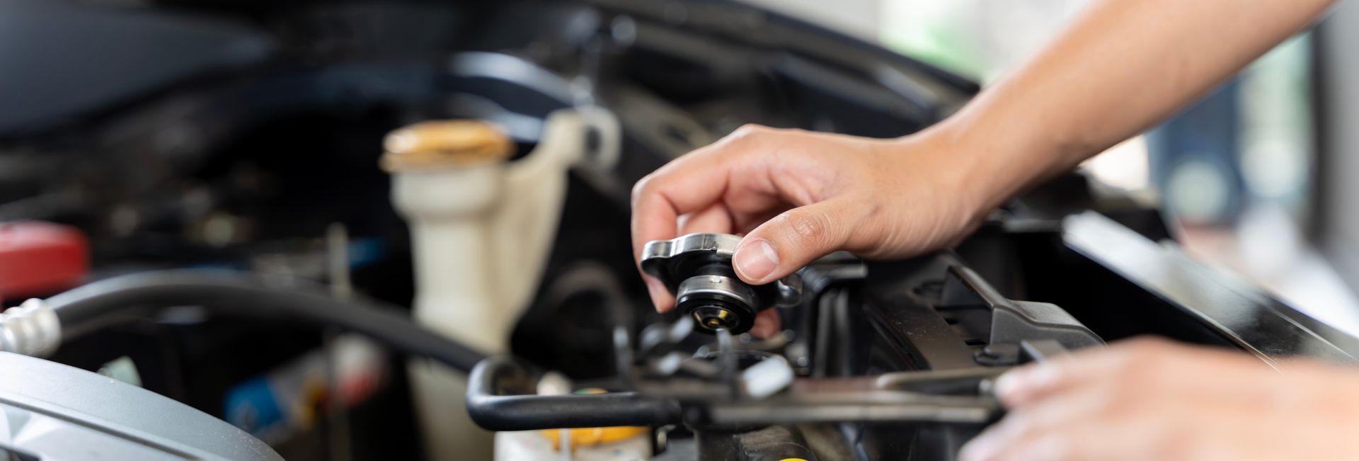 A person's hands turning the radiator cap on a car engine.