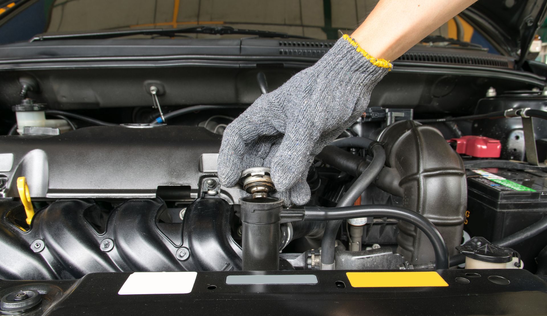 A hand wearing a gray glove is checking a car engine’s radiator cap.