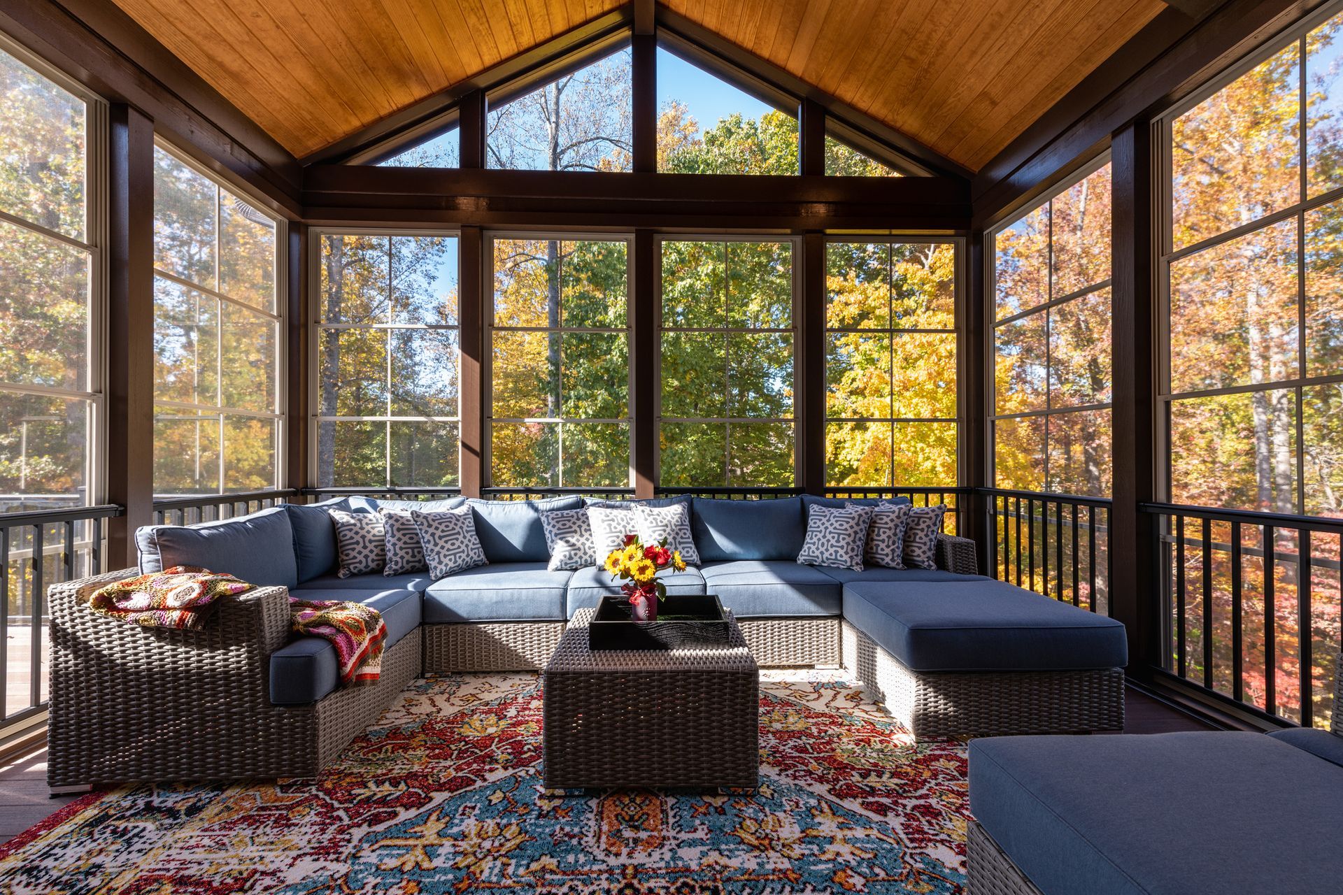 Cozy screened-in porch with blue sectional, patterned rug, and a view of fall foliage.