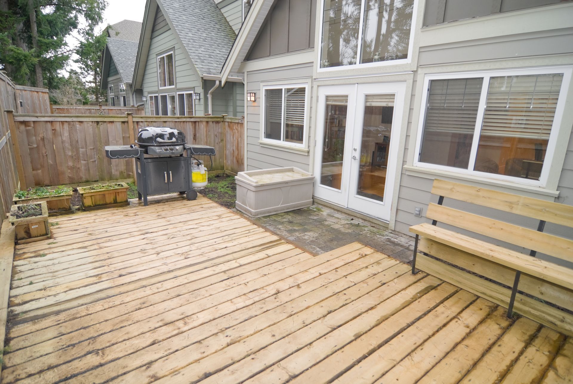 Backyard deck with grill, bench, and access to a house with double doors and windows.