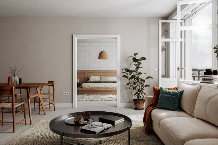 A bright living room with a sofa, round coffee table, and dining table; a bedroom visible through a doorway.