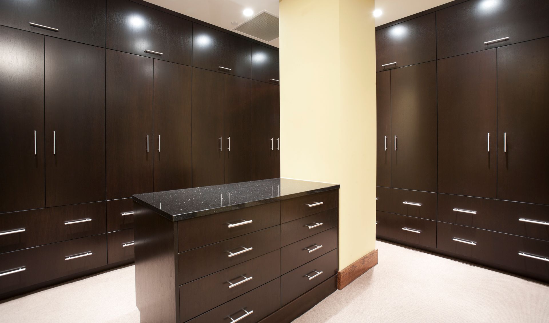 Walk-in closet with dark wood cabinets, a central dresser, and beige walls.