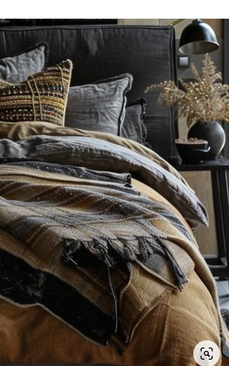 Cama con manta estampada en tonos mostaza y negro, almohadas y cabecero negro.