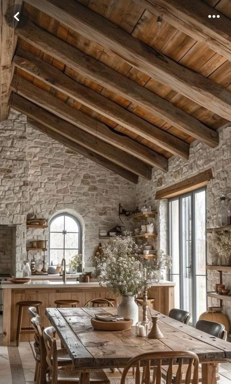 Comedor rústico con paredes de piedra, vigas de madera y una larga mesa de madera.
