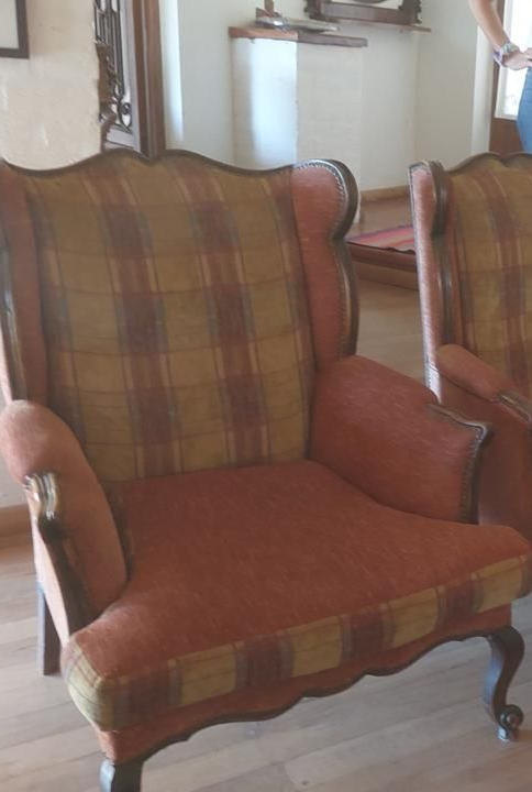 Sillón orejero tapizado en tela de cuadros, con una silla adyacente visible.