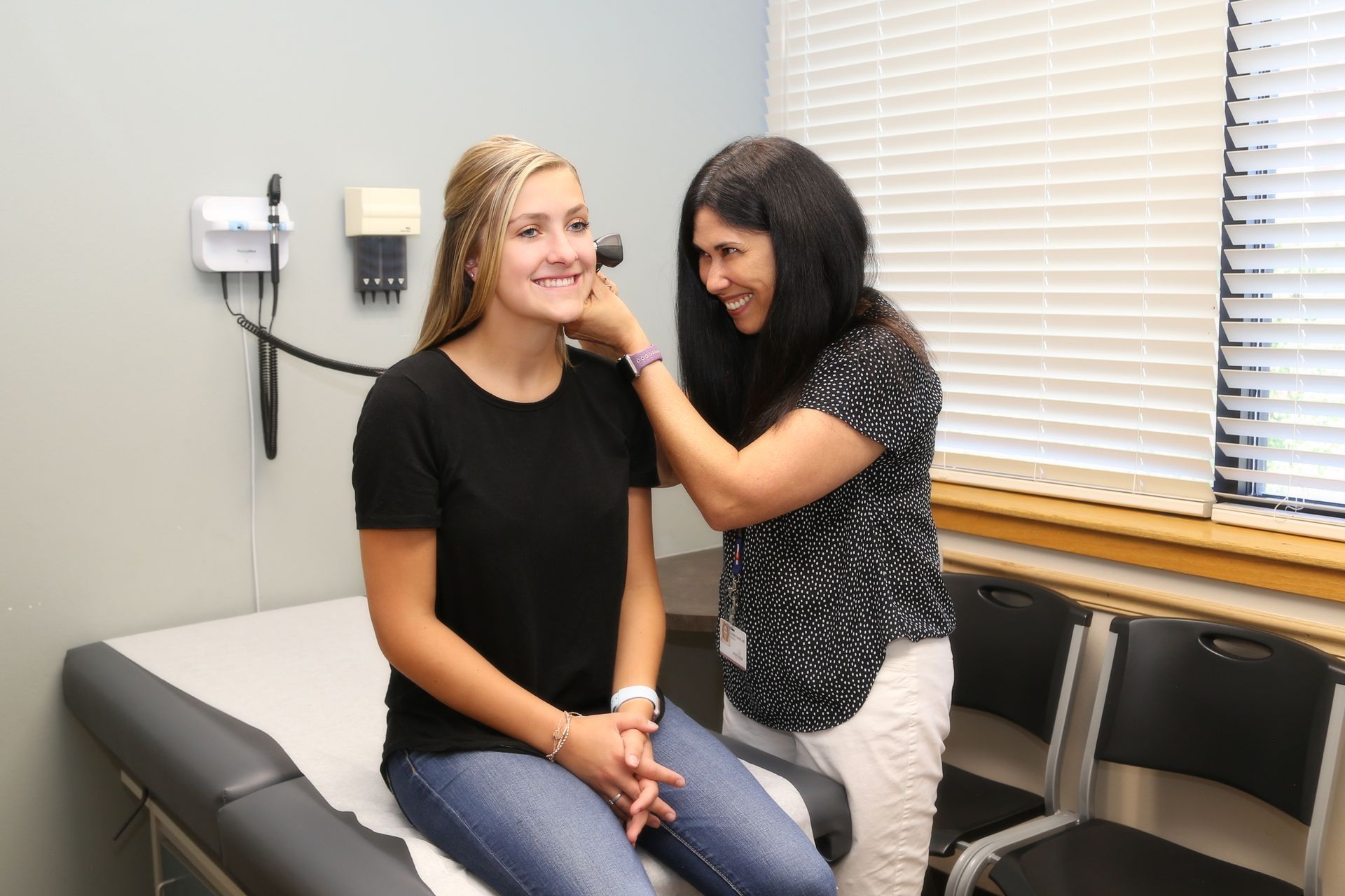 A woman is examining another woman 's ear in a doctor 's office.