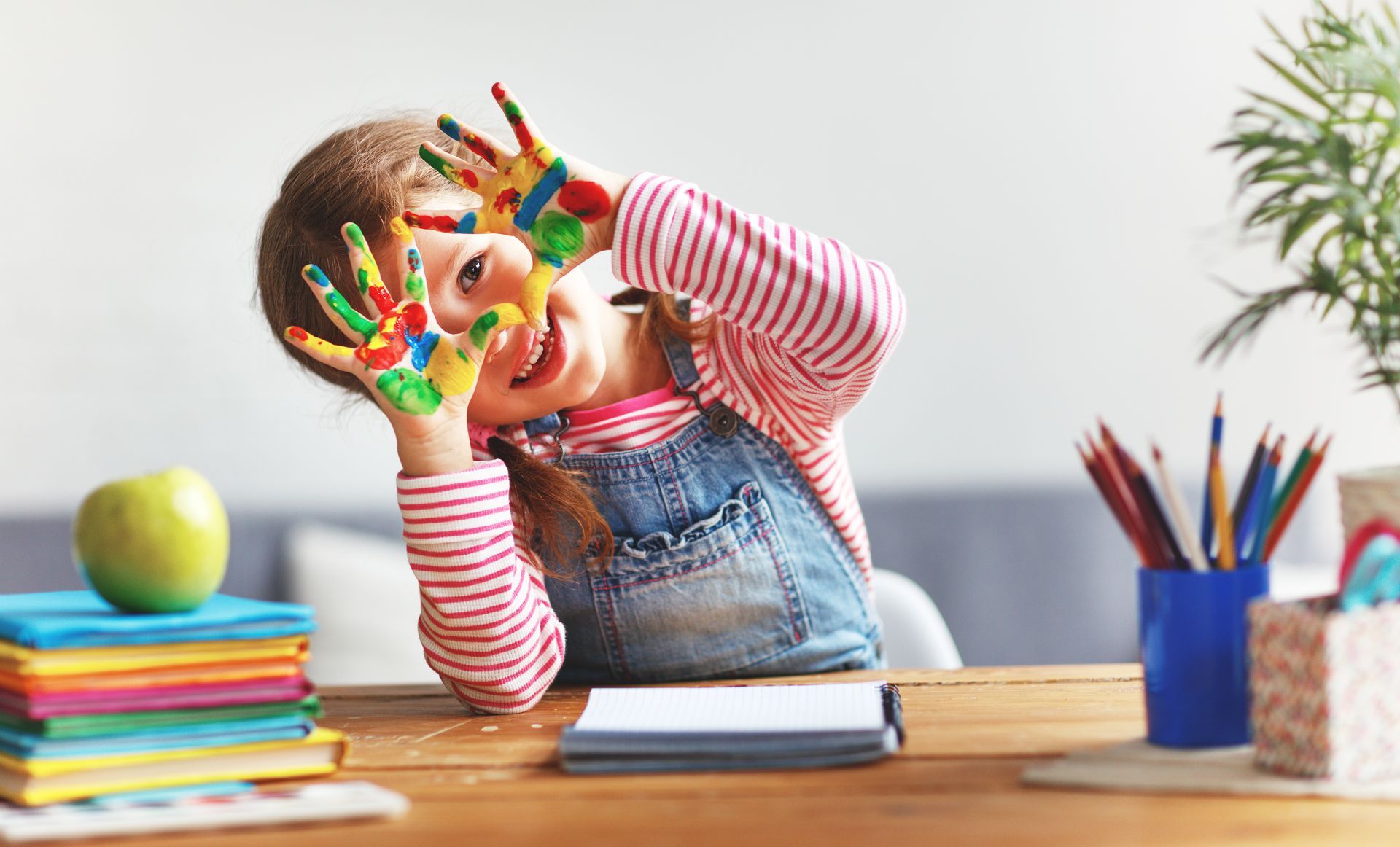 A little girl is sitting at a table with her hands painted.