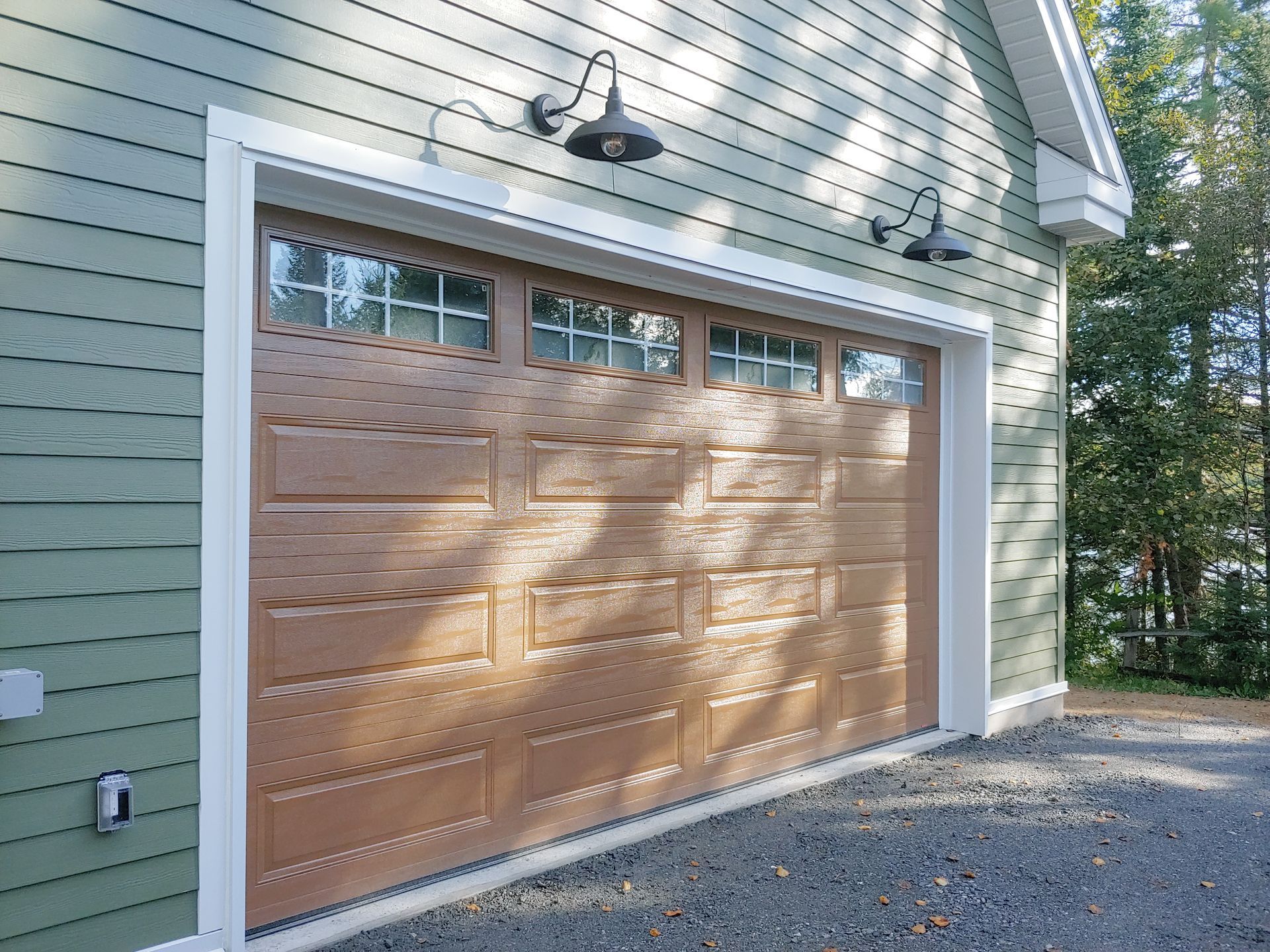 Porte de garage brune avec fenêtres, revêtement vert et lumières noires.