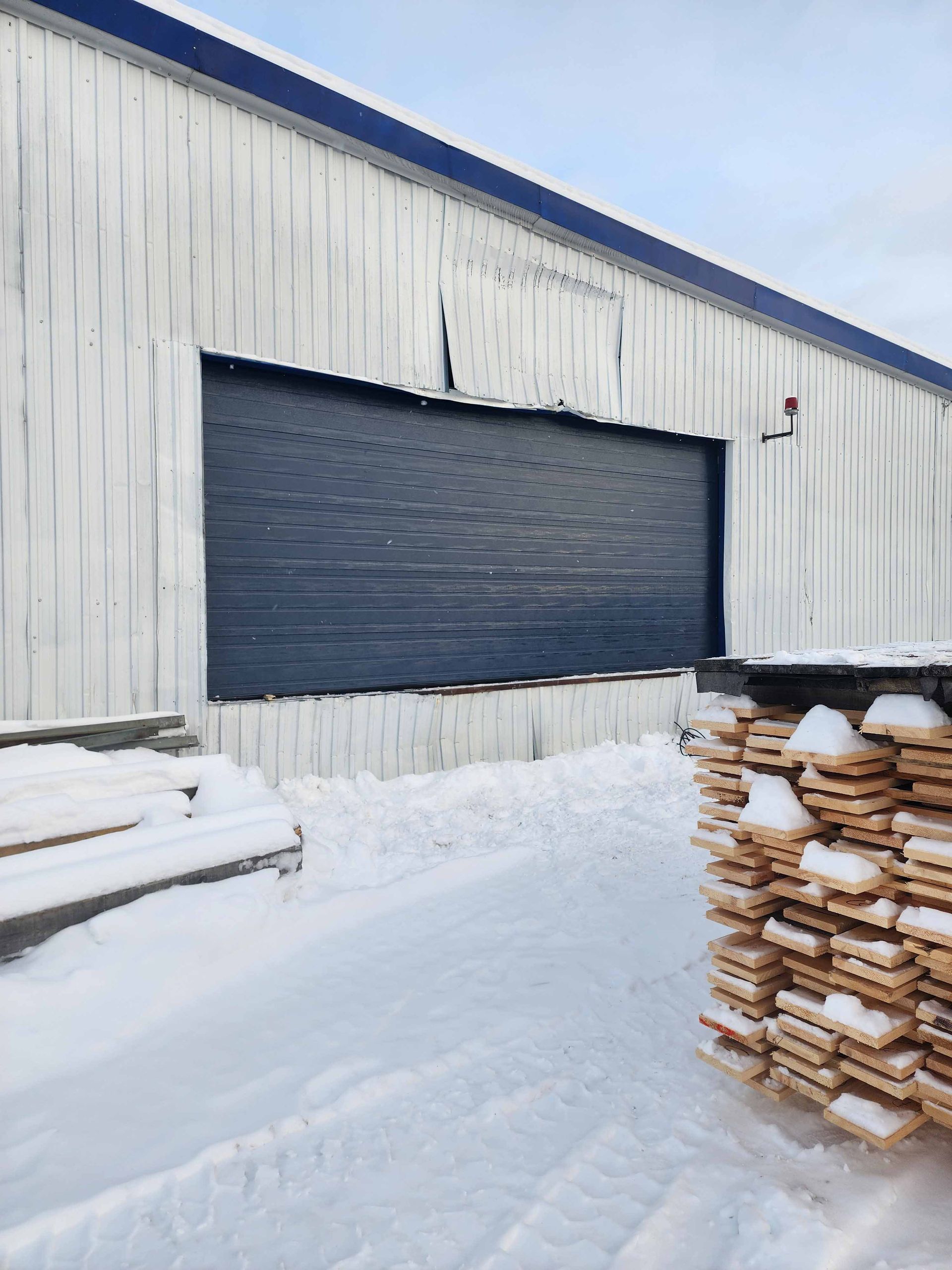 Un bâtiment blanc avec une porte bleue et une pile de bois devant
