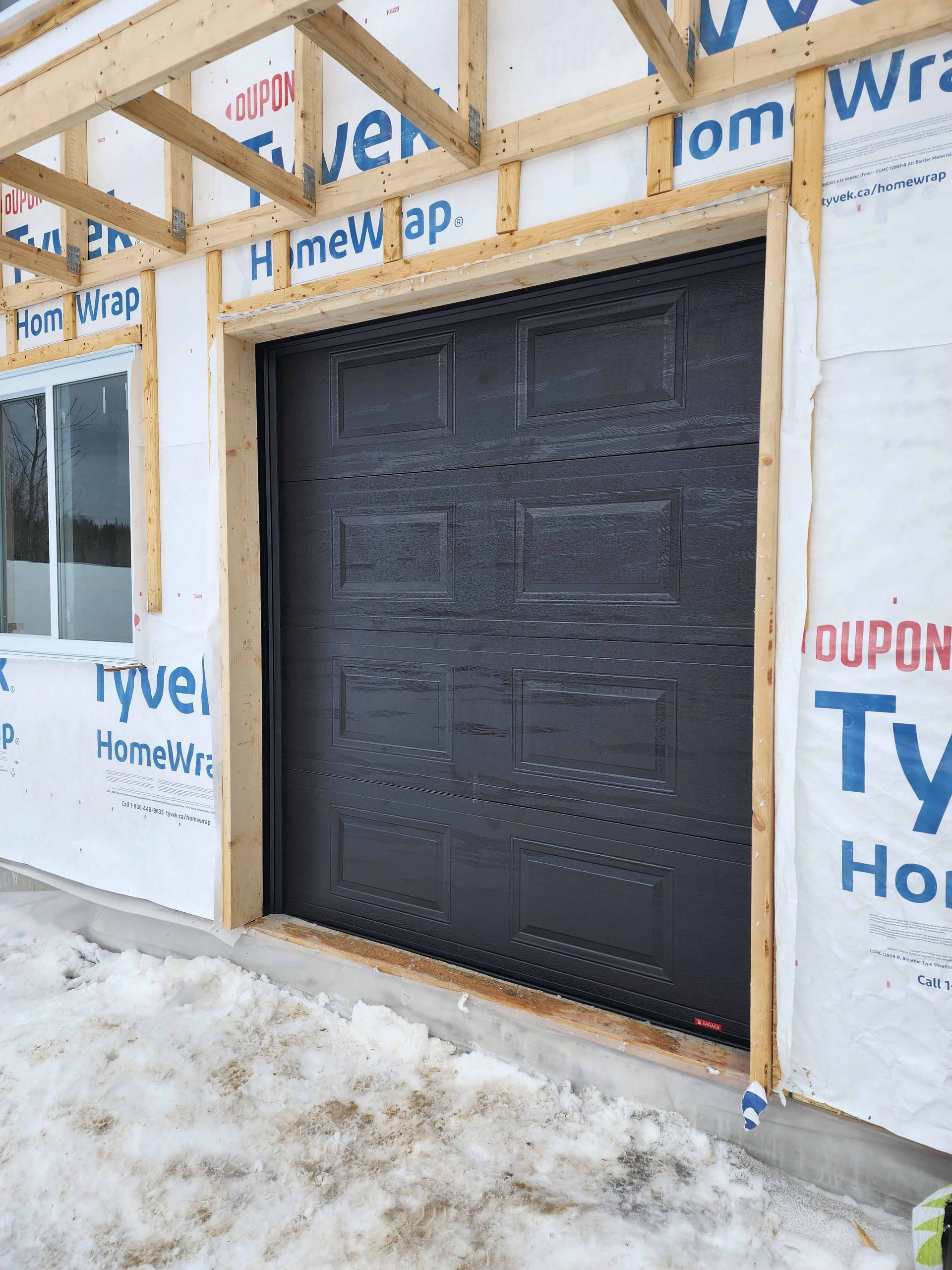 Une porte de garage noire est en cours d'installation sur le côté d'une maison.