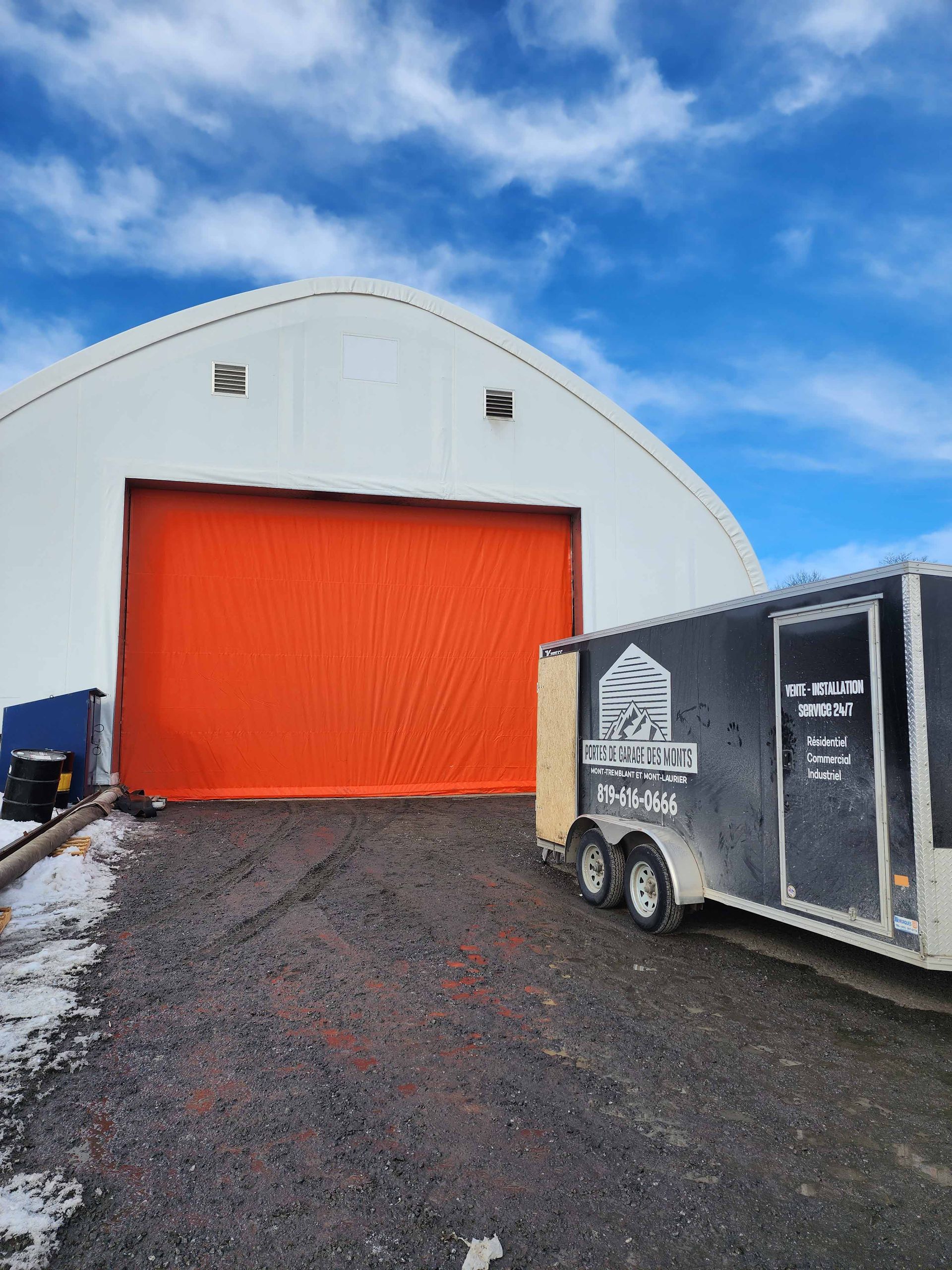 Une remorque est garée devant un grand bâtiment avec une porte orange.