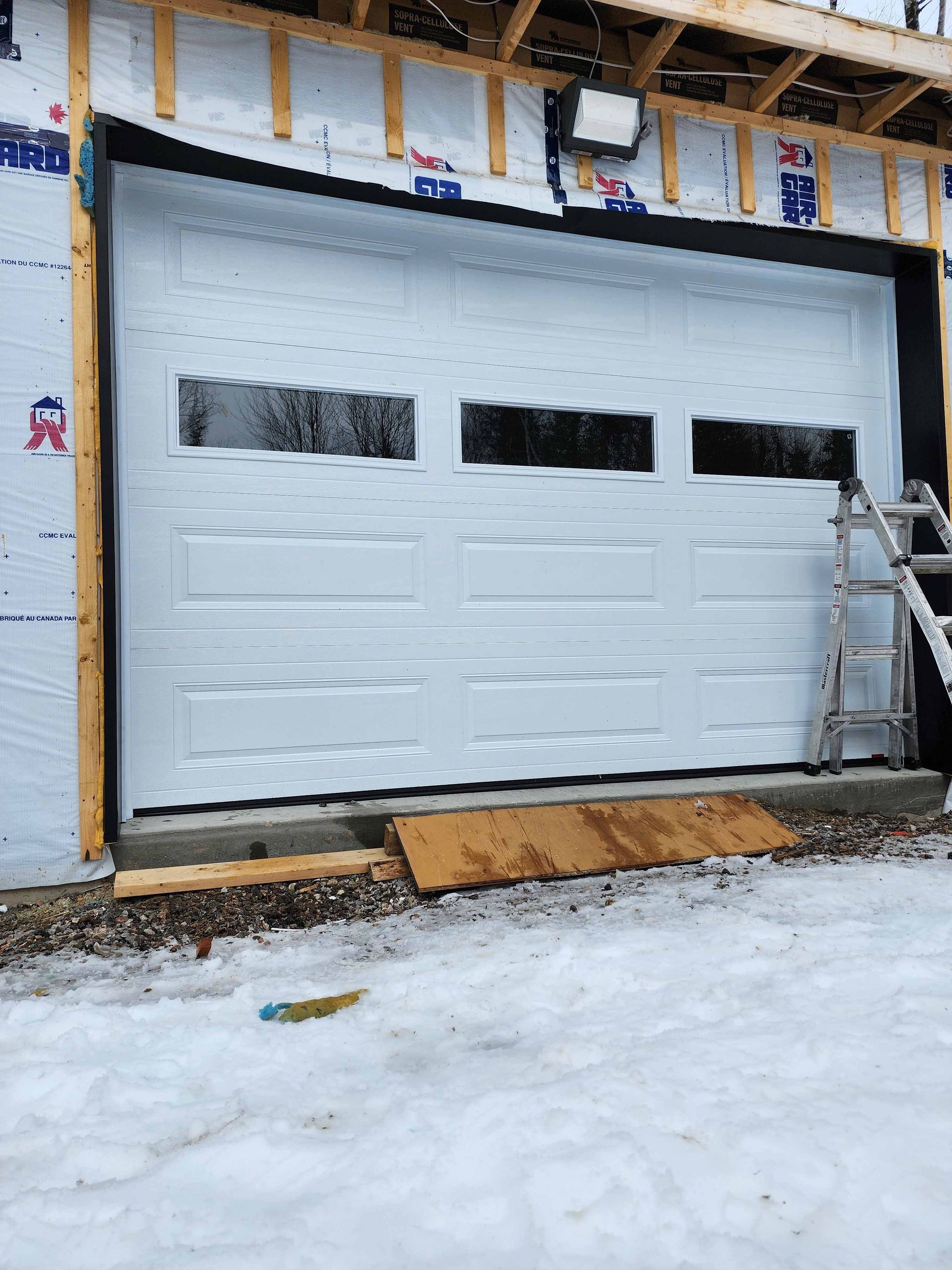 Une porte de garage blanche est en cours d'installation dans la neige.