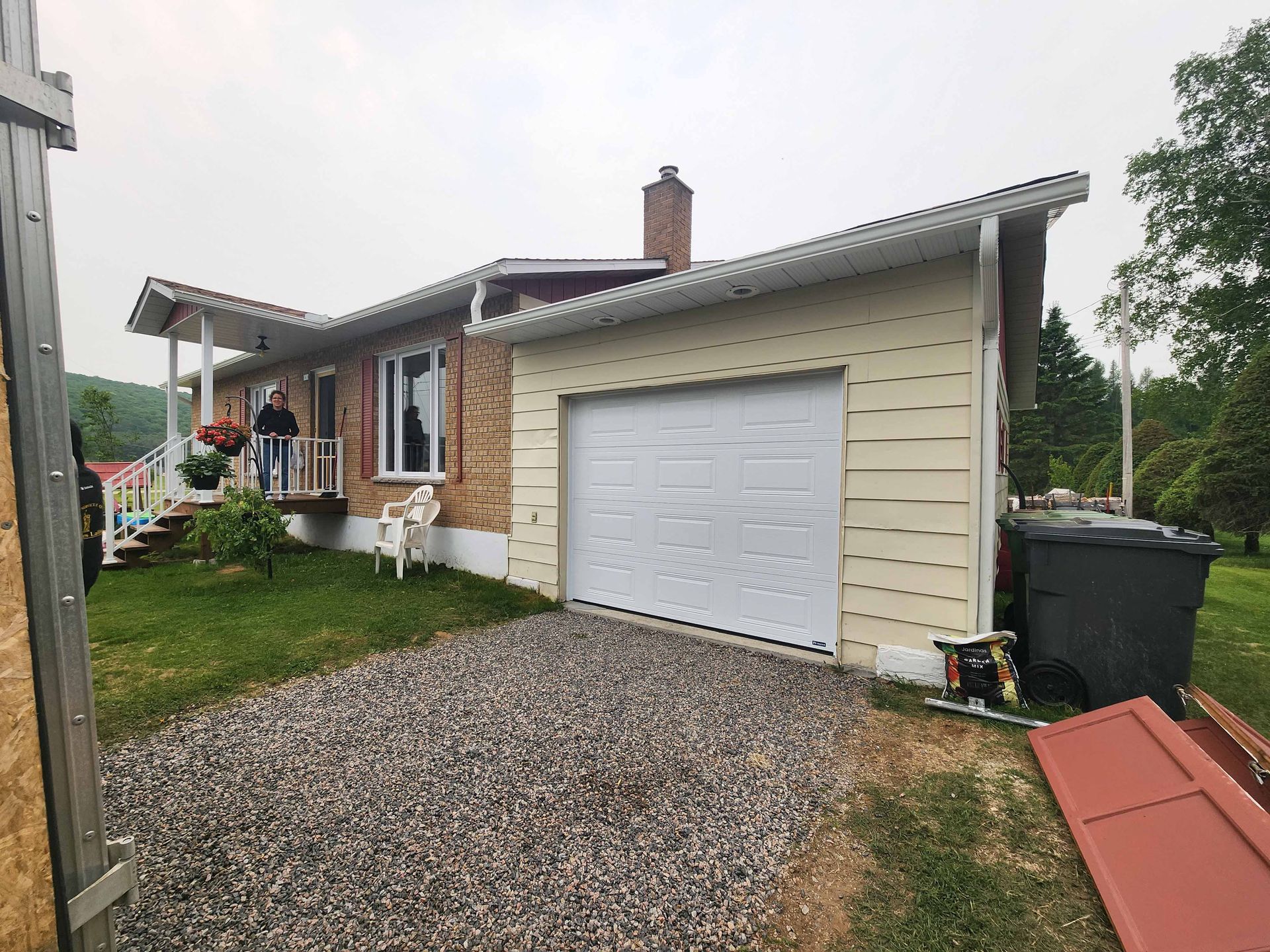 Un homme se tient sur le porche d'une maison avec une porte de garage.
