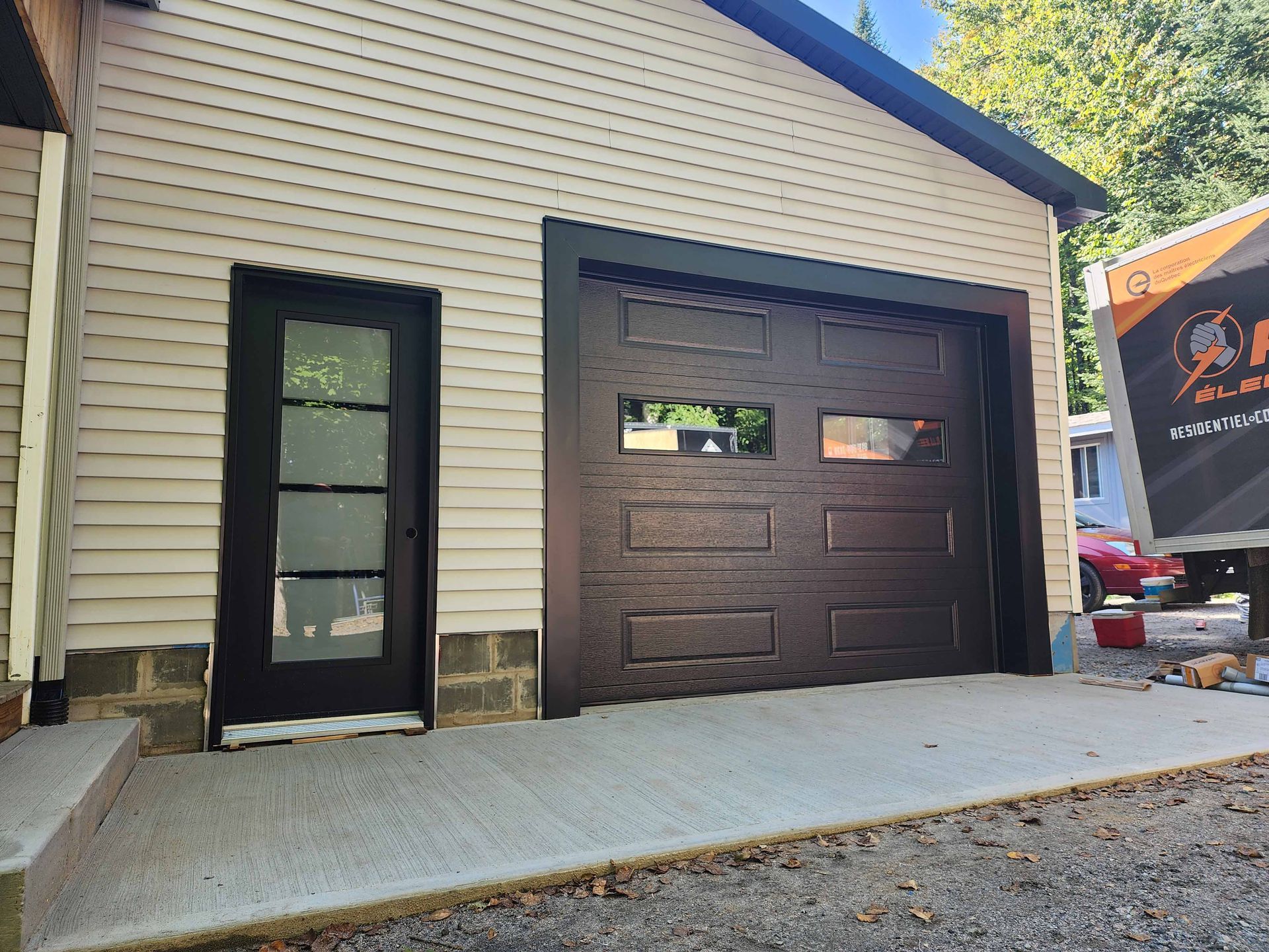 Extérieur du garage avec porte brune et porte de garage, à côté d'une porte à cadre noir.