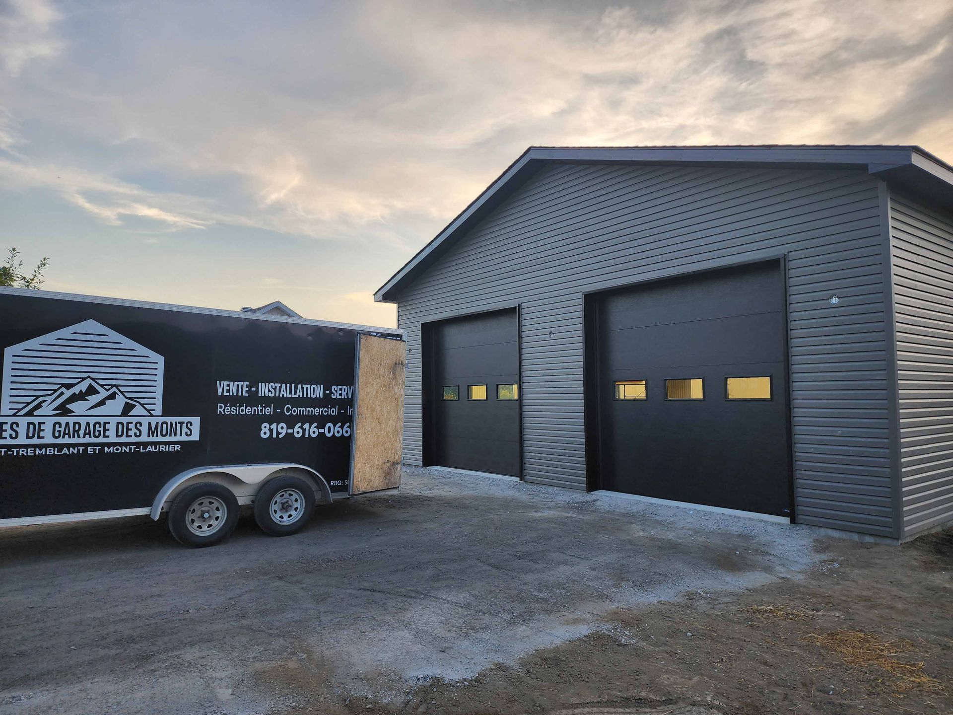 Une remorque noire est garée devant un garage.
