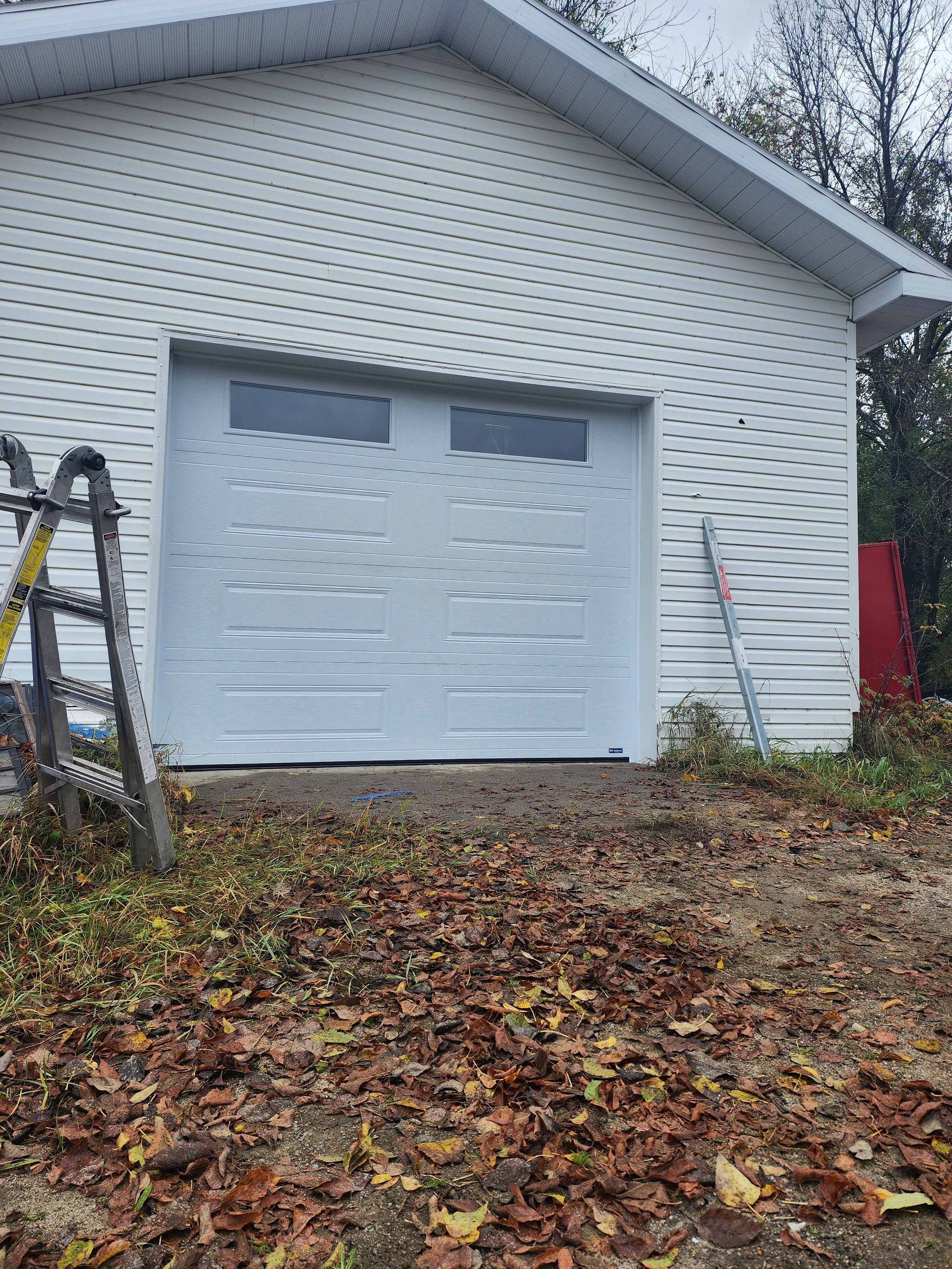 Garage blanc avec porte fermée, deux fenêtres en haut et échelle en aluminium à gauche.